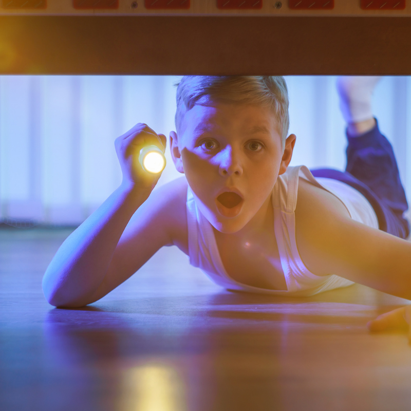 un garcon sous son lit avec une lampe